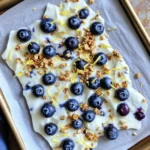 - 2 cups plain Greek yogurt - 1/4 cup honey or maple syrup - Zest of 1 fresh lemon - 2 tablespoons freshly squeezed lemon juice - 1 cup fresh blueberries - 1/2 cup granola - A pinch of sea salt - Alternative sweeteners - Different fruit options - Nut or seed additions The main ingredients create a bright and tangy flavor. Greek yogurt gives a creamy base. Honey or maple syrup adds sweetness. The lemon zest and juice bring a refreshing twist. Fresh blueberries burst with flavor and color. Granola adds crunch and texture. A pinch of sea salt balances it all. You can customize this treat in many ways. Try using agave or stevia as sweeteners. Swap blueberries for strawberries or raspberries for a new taste. Add nuts like almonds or seeds like chia for extra crunch. The options let you play with flavors and textures. This recipe is easy to follow. You can find the Full Recipe to get all the details. It’s a fun way to explore healthy snacks while enjoying a delicious treat! - Line a baking sheet with parchment paper. - Combine Greek yogurt with honey, lemon zest, juice, and salt. To start, grab your parchment paper. Lay it on a baking sheet. This makes it easy to lift the finished bark off later. Next, in a large bowl, mix the Greek yogurt, honey, lemon zest, lemon juice, and a pinch of salt. Stir until it’s nice and smooth. This yogurt base is the heart of your bark. - Pour and spread yogurt mixture onto the baking sheet. - Add blueberries and granola. Now, pour the yogurt mix onto your lined baking sheet. Use a spatula to spread it out evenly. Aim for about a half-inch thick layer. Then, take your fresh blueberries and sprinkle them over the top. Press each one gently into the yogurt. This helps them stick. Finally, add your granola on top. This gives it a great crunch. - Transfer to the freezer for 3 hours. - Break into pieces and serve. Next, slide the baking sheet into the freezer. Let it freeze for about three hours. Once it’s fully frozen, take it out. Peel the bark from the parchment paper. You can break it into pieces or cut it into squares. Now, it’s ready to enjoy! To get a smooth yogurt mixture, start with room temperature yogurt. This makes it easier to mix. Use a whisk or spatula for best results. Mix until no lumps remain. For freezing, spread the yogurt mixture evenly on the baking sheet. Aim for about 1/2 inch thick. This thickness helps it freeze well. Make sure to press the blueberries down gently. This helps them stick better. Freeze for at least 3 hours. This gives the bark a good firm texture. When serving, place the yogurt bark on a nice platter. Drizzle with honey for extra sweetness. You can also sprinkle more lemon zest on top. This adds a pop of color and flavor. This yogurt bark pairs well with other snacks. Try serving it with fresh fruit or nuts. It also goes great with granola cups. These add a crunchy contrast. One mistake is over or under mixing the yogurt. If you over mix, the texture can become too thin. If you under mix, lumps can form. Both can ruin the final product. Another mistake is choosing the wrong type of granola. Select a granola that you enjoy. A sweet or nutty blend can add great flavor. If it is too sweet, it may overpower the yogurt’s taste. {{image_4}} You can change the taste of your Lemon Blueberry Greek Yogurt Bark with ease. Try adding other citrus fruits like lime or orange. These bright flavors really pop and keep things fun. You can also use mixed berries such as strawberries, raspberries, or blackberries. Seasonal fruits work well too. Think peaches in summer or apples in fall. Each fruit brings its own unique taste. If you follow a vegan diet, you can swap the Greek yogurt for a dairy-free yogurt. Coconut or almond yogurt makes a great choice. Just make sure to pick one without added sugars. If you want to cut the sugar, use a sugar substitute like stevia or erythritol. This way, you can enjoy your treat without the extra calories. You can make your yogurt bark even richer. Adding nut butters like almond or peanut butter gives a creamy texture. Drizzling melted dark chocolate on top adds sweetness and depth. If you want to boost nutrition, try adding seeds like chia or flaxseed. They offer healthy fats and fiber without changing the taste much. For the Full Recipe, you can find all the steps to make this refreshing treat. To keep your Lemon Blueberry Greek Yogurt Bark fresh, use an airtight container. This helps prevent freezer burn. Make sure the container is clean and dry before adding the bark. If you have a lot, layer pieces between parchment paper to avoid sticking. For freezing, place the bark in your freezer for a quick freeze. When you're ready to enjoy it, thaw the pieces in the fridge. This method keeps the texture smooth and creamy. If you're in a hurry, you can let it sit at room temperature for a few minutes. In the freezer, your yogurt bark stays fresh for about two months. After that, it may lose flavor and texture. To know if it has spoiled, look for ice crystals or an off smell. If it looks or smells funny, it's best to toss it. Enjoy your treat while it's fresh! It takes about 3 hours to freeze your yogurt bark. This time lets it become firm and ready to eat. For the best results, I suggest leaving it in the freezer for a bit longer if you can. A few extra hours won’t hurt. Just make sure it is solid before you take it out. Yes, you can use frozen blueberries. The pros are that they are easy to find and have a longer shelf life. They can also add a nice chill to the bark. However, the cons include that they may release extra juice. This can make the yogurt mixture a bit watery. If you use frozen berries, let them thaw a bit before adding them. This recipe is very easy to customize. You can change the sweetness by using different sweeteners. If you want to try other fruits, feel free to swap in strawberries or raspberries. You can even add nuts or seeds for extra crunch. Mix it up and make it your own! Check the full recipe for more ideas. This blog post shared a simple recipe for lemon blueberry Greek yogurt bark. You learned about the key ingredients, preparation steps, and tips for success. Customization options let you change flavors or ingredients to suit your taste. You can store your creations for months, ensuring a tasty snack is always ready. Enjoy making this treat. Your own twist will make it even better!